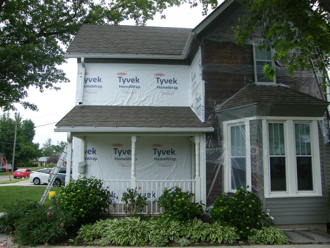 The porch wall wrapped while the upper east wall waits, the old cedar still exposed under sheeting.