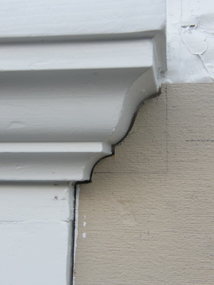 The siding cut to follow the cornice profile, cut by cut, where the two meet.